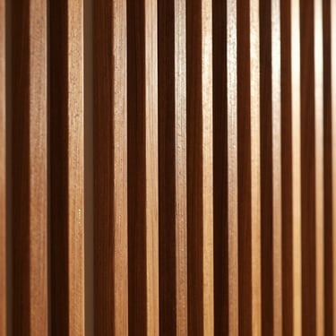 Close-up of vertical walnut wood slats (lambrin), warm amber wood grain, soft shadow lines, interior design detail