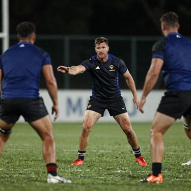Action shot of a male rugby coach gesturing and directing plays on a pitch during an evening training session.