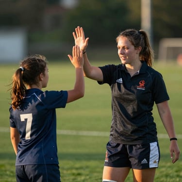 Candid shot of a female youth rugby coach high-fiving a young player on a green field during golden hour.