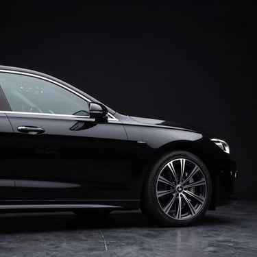 Studio low-key lighting highlighting the sleek profile of a modern black luxury sedan, clean black background, metallic reflections.