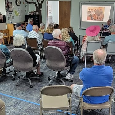 A group of senior citizens attending a community presentation with a projector screen in a meeting room.