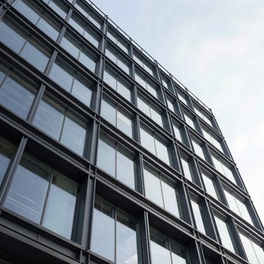 Low-angle shot of a modern commercial mid-rise with exposed steel framing and geometric glass panels.