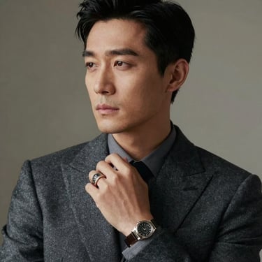 A portrait of a refined man in a charcoal tailored suit, looking thoughtfully into the distance, with the focus on a handcrafted signet ring on his finger.