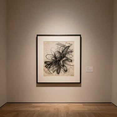 A minimalist gallery wall featuring a single framed charcoal drawing on textured paper, hung in a spacious room with warm plaster walls.