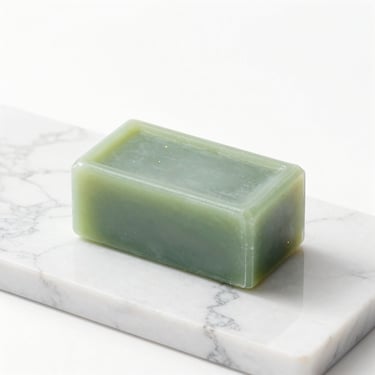 A clean, solid geometric soap bar on a white marble surface, soft green accents.