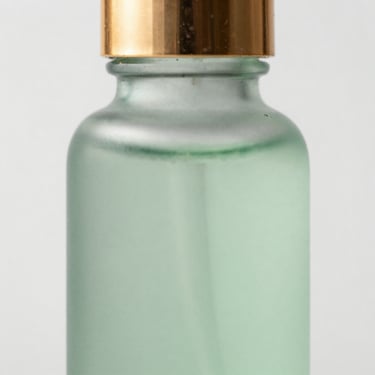 Macro close-up of a frosted light-green serum bottle, clinical studio lighting, soft gold reflections.