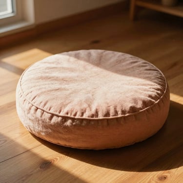 A minimalist round meditation cushion made of natural linen fabric, warm golden-hour light streaming onto a wooden floor