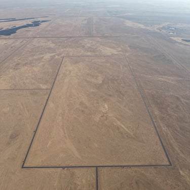 High-altitude drone photograph of a flat rectangular desert land parcel with superimposed digital boundary lines, crisp morning light, high detail.