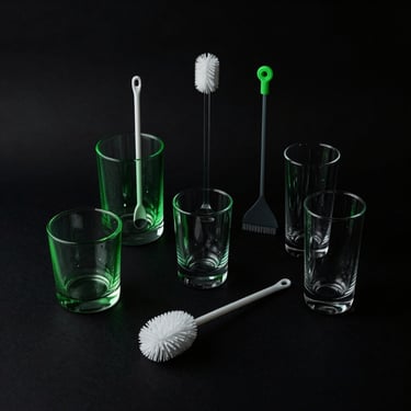 Curated glass accessories and cleaning tools arranged on a dark minimalist surface, dramatic low-key lighting, neon green rim light