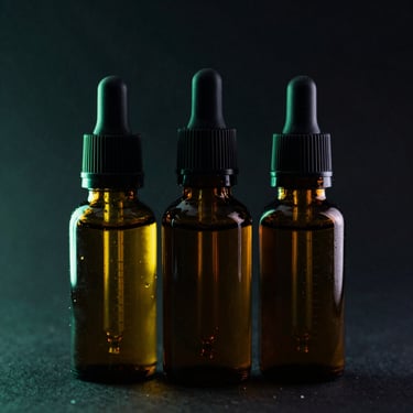 Three amber glass e-liquid bottles with dropper caps, aligned on a dark textured background, dramatic green rim lighting, sharp macro details