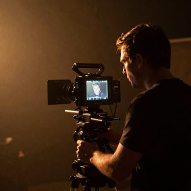 A film director looking through a camera monitor on a dark, atmospheric set with warm amber backlighting