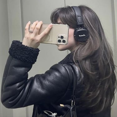 Woman with long brown hair taking mirror selfie wearing black leather puffer jacket