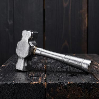 Heavy aluminum meat hammer and solid pestle resting on a dark wood block, high-contrast metal textures.