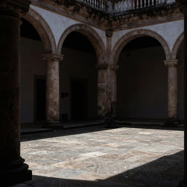 Low-key architectural geometry of a colonial courtyard in Cosme Velho, shadows stretching across stone floors, quiet and sober atmosphere.