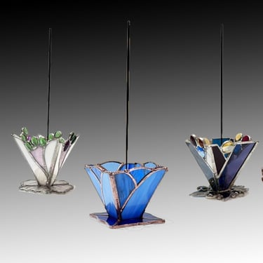 A collection of five stained glass incense holders in various floral shapes and vibrant colors, each with an incense stick