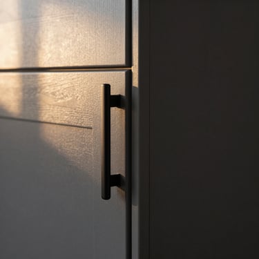 Close-up detail of flat-panel cabinet door corner joint and matte black pull hardware, dark charcoal finish, golden-hour window light raking across surface showing finish texture, tight reveal gap visible — no people