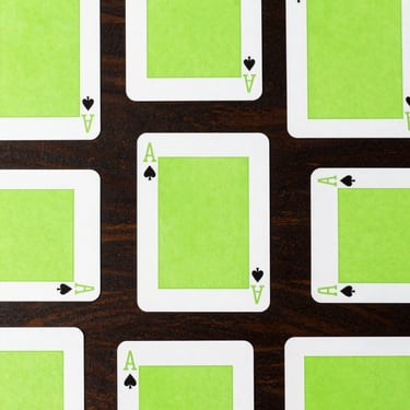 Overhead flat-lay of minimalist playing cards with bold typography and neon green accents spread on a dark wooden table.
