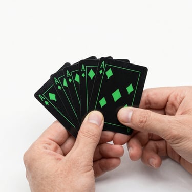 Close-up of hands holding a tiny deck of black cards with vibrant green icons under sharp studio lighting.