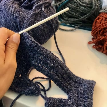 Proceso de tejido de un sueter de muñeca a crochet color azul marino con madejas de estambre al fondo