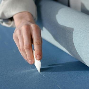 Una mano con gis de para marcar corte en tela, la tela es color azul y se está marcando la línea de corte