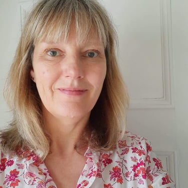Profile of a middle aged woman with short blonde hair wearing a floral pink shirt