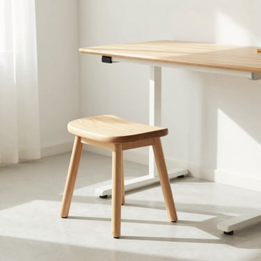 An ergonomic wooden stool next to an oak standing desk, bright airy room, soft shadows, minimalist home setting, 35mm