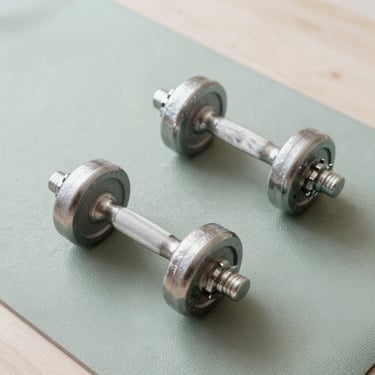 Top-down view of adjustable steel dumbbells resting on a clean sage green workout mat, bright daylight, minimal home setting, 35mm