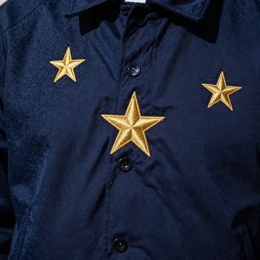 Close-up of embroidered gold stars on a deep navy blue streetwear jacket, dramatic studio lighting.