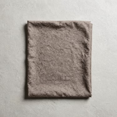 Overhead flat-lay on pale concrete, a folded merino running buff in deep charcoal laid flat with subtle texture visible, natural daylight from one side, minimal props, clean background