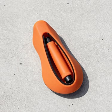 Overhead flat-lay on pale concrete, a small orange silicone cycling saddle bag unzipped to reveal a spare tube and tyre lever inside, natural daylight, clean shadows, no extra props