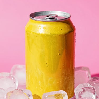 Vibrant pop-art close-up of a bright yellow-orange soda can on ice, set against a hot pink background, high-contrast direct sunlight