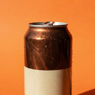 Vibrant pop-art close-up of a classic brown and cream soda can, set against a solid bright orange background, direct harsh sunlight, sharp shadows