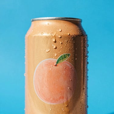Vibrant pop-art close-up of a golden peach-colored soda can with condensation, set against a solid electric blue background, direct harsh sunlight