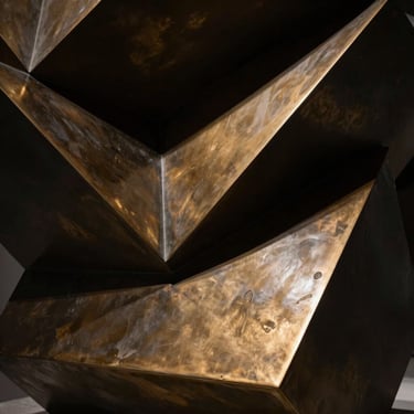 Extreme close-up of a polished bronze geometric sculpture, sharp architectural shadows, high contrast