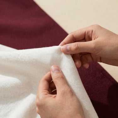 Editorial close-up of hands gently holding an organic cotton fabric, warm natural light, soft shadows