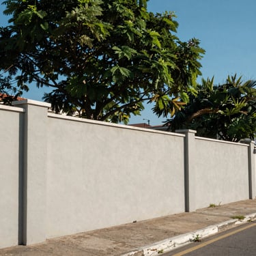 Lote residencial plano cercado por muros limpos e árvores ao fundo sob céu azul