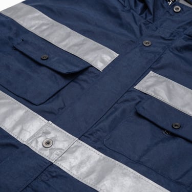 Macro close-up of a heavy-duty navy blue industrial raincoat set with double-stitched sealed seams and high-visibility reflective strips.