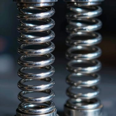 Extreme close-up of a high-tension compression spring, steel wire coils reflecting cold studio light, dark background