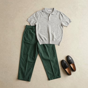 Aesthetic flat-lay of a casual outfit: dark green trousers, light grey knit polo, and minimalist leather loafers, soft natural light