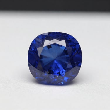Extreme macro of a cushion-cut Ceylon sapphire on a white light table, controlled raking studio light revealing velvety blue saturation and silk inclusions, white negative space dominating the frame