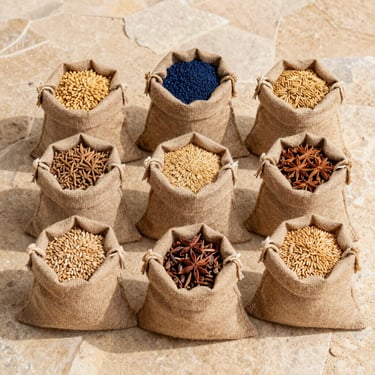 Flat-lay of organic agricultural commodities, raw grains and spices in natural burlap sacks on a warm sand-colored stone background, sharp daylight