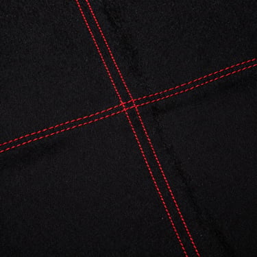 Gritty close-up texture shot of heavyweight black cotton fabric with raw red stitching, direct flash, high contrast, harsh shadows