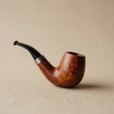 Clean studio photo of a hand-carved wooden curipe pipe, V-shaped, with delicate geometric carvings on a neutral sand background, soft depth of field