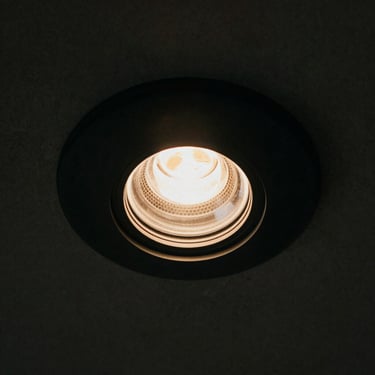 Extreme close-up of a matte black recessed linear downlight, showing its deep-set baffle and honeycomb louver, dark background.