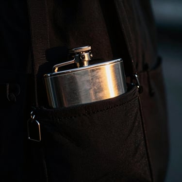 Tight macro detail of a sleek black bottle bag holding a metal flask, neon gold highlights, high contrast, 35mm