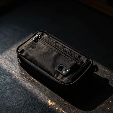 Compact black tech pouch and everyday essentials on a dark metallic surface, high contrast, 35mm