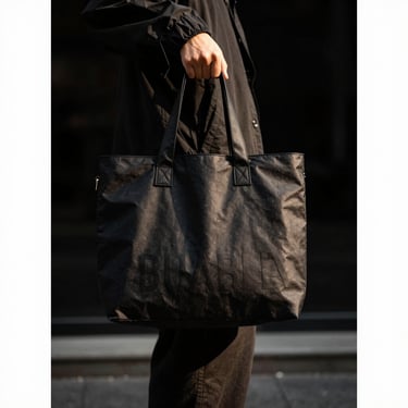 Durable black shopping tote bag held by a person in streetwear, urban backdrop, high contrast, 35mm