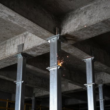 Low-angle shot of adjustable steel shoring props supporting a concrete formwork ceiling on a construction site, dramatic industrial shadows, sharp focus, 1:1 square aspect