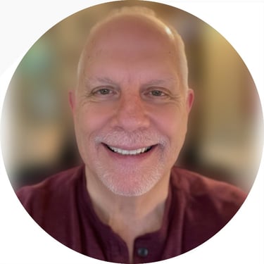 Headshot of a smiling bald man with a grey goatee wearing a maroon shirt.