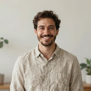 Unposed portrait of a professional male therapist in a neutral linen shirt, smiling warmly in a sunlit studio, soft diffused coastal light, shallow depth of field